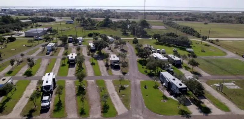 Aerial view of Bay Breeze RV Park showing rows of RV sites along gravel drives, with the bay and Port O'Connor in the background