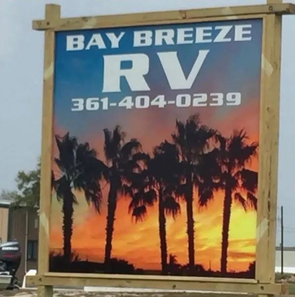 The Bay Breeze RV sign at the roadside, a painted sunset behind palm trees with the phone number (361) 404-0239